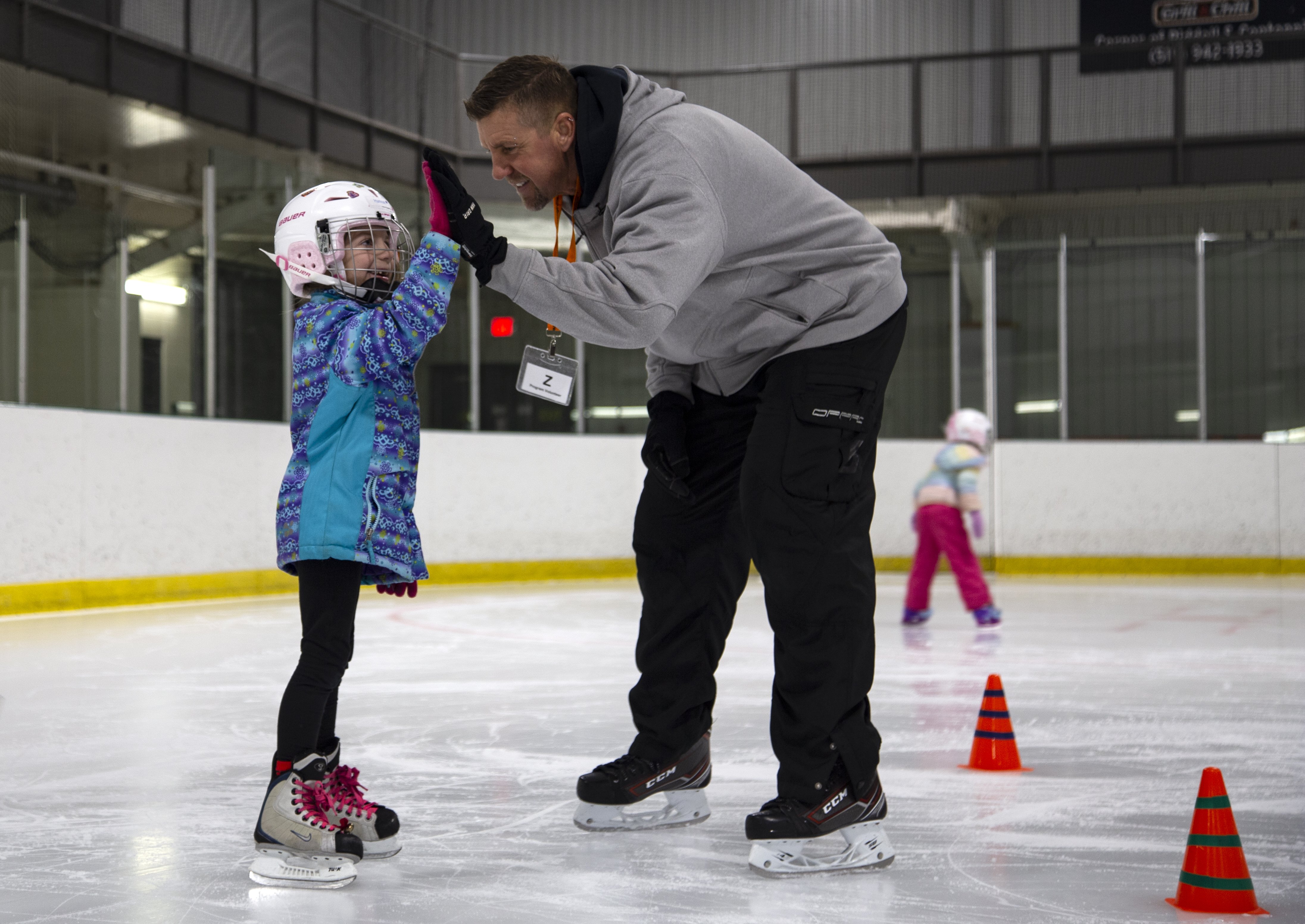 A skating instructor high fives a child learning to skate